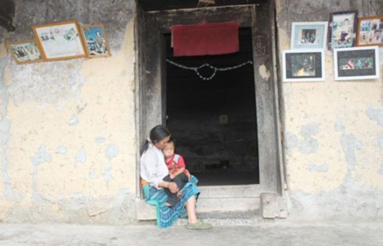 Vợ anh Púa ôm con ngồi trên bậu cửa, hình ảnh quen thuộc của những người phụ nữ Mông. 